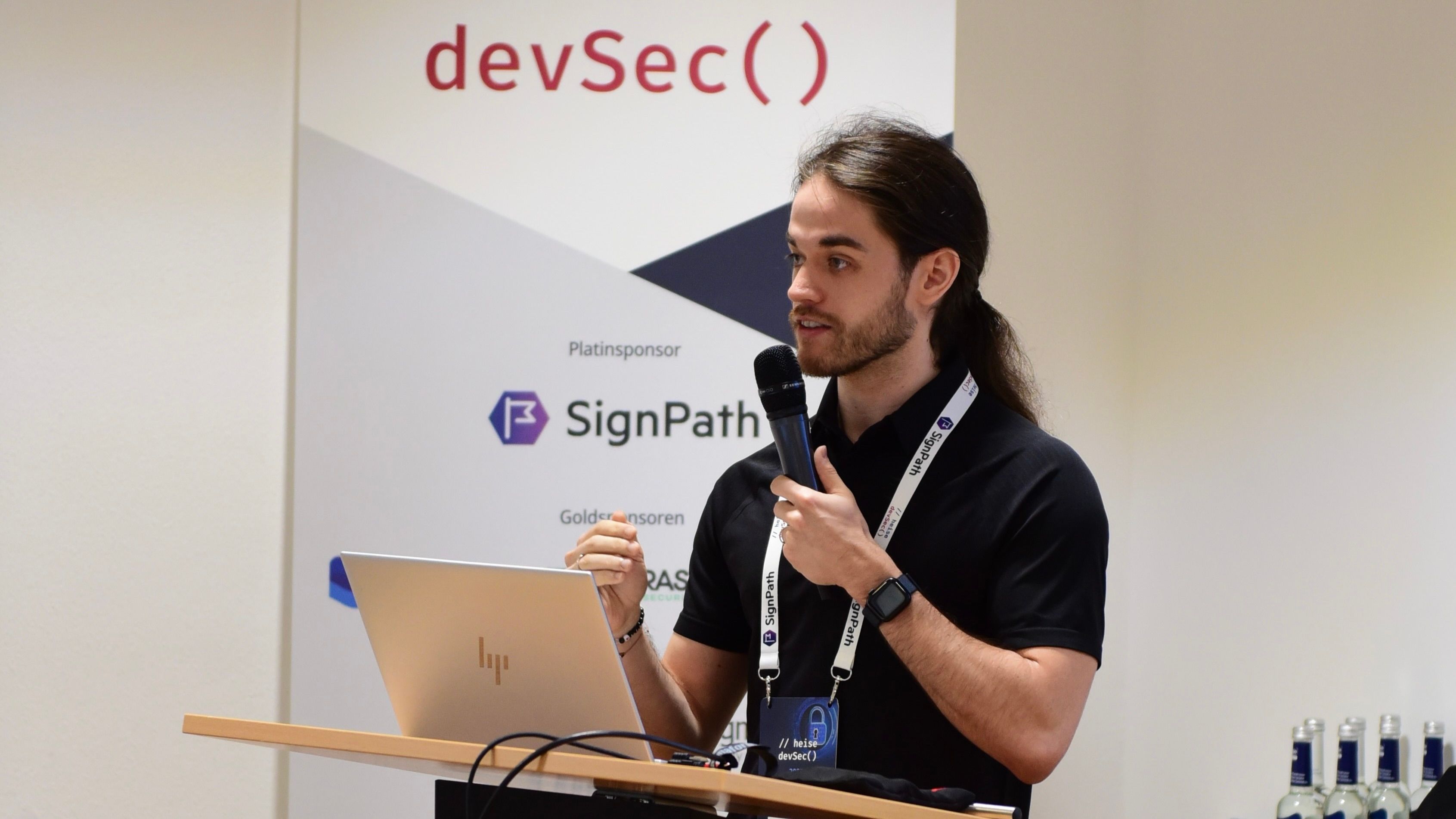Me speaking at Heise devSec 2025. I’m holding a microphone and looking at the audience.