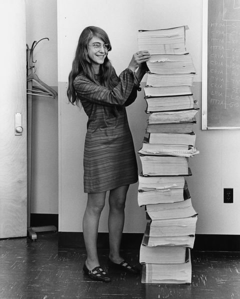 Margaret Hamilton standing next to a stack of paper with the source code for the Apollo Guidance Computer.
