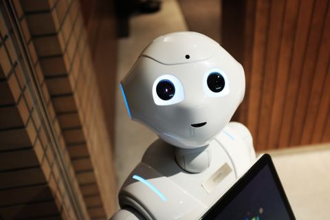 A white robot with a friendly face looking at the camera, holding a tablet.